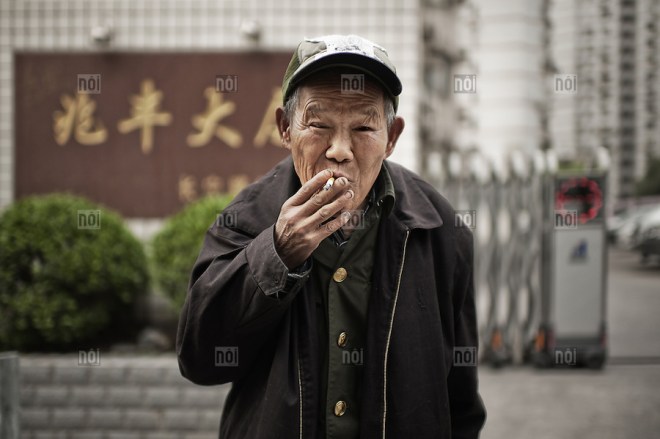 Blind old man smoking a cigarette in a street of Shanghai, China